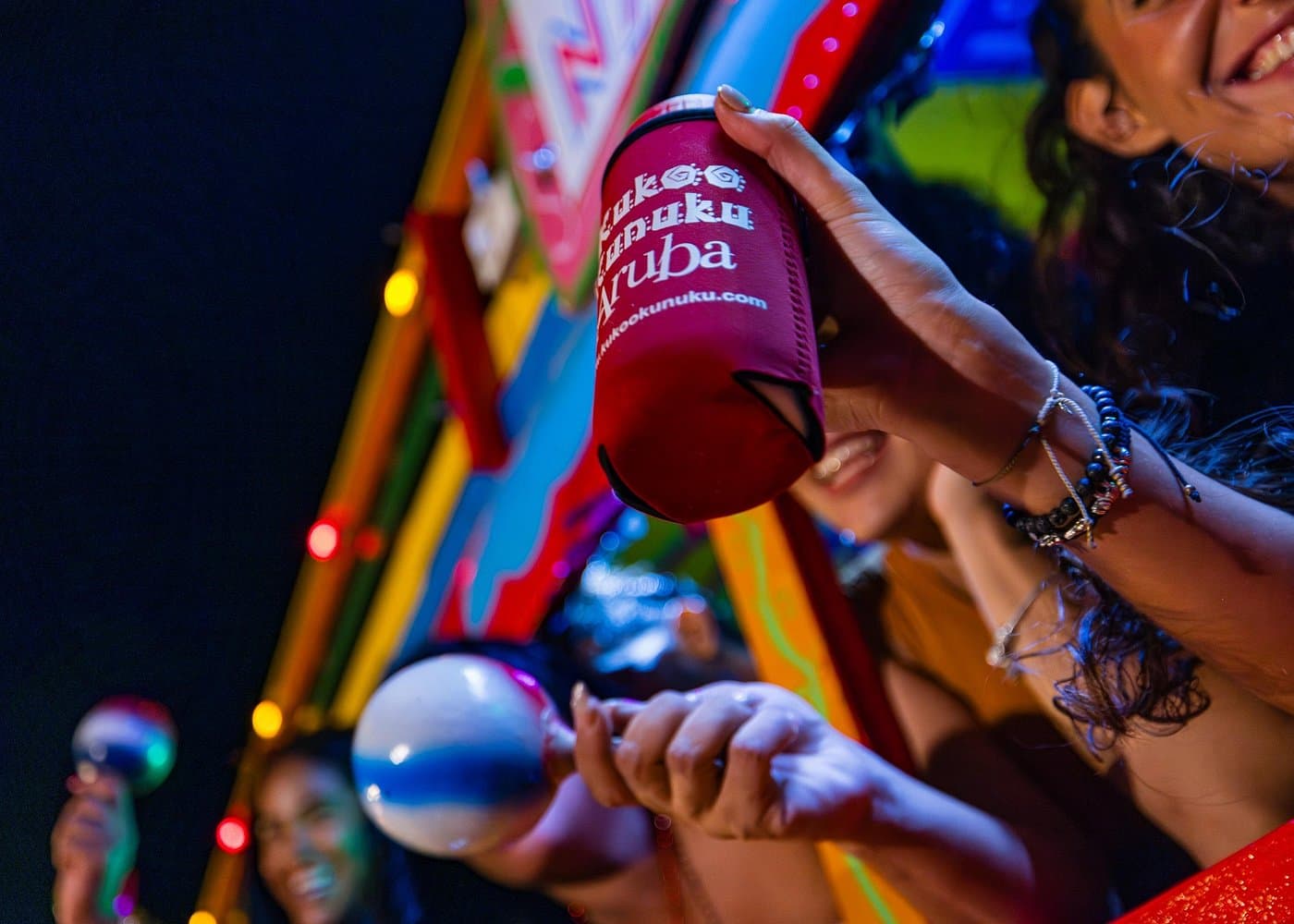 A red Kukoo Kunuku Aruba drink koozie and maracas on the open-air party bus at night.