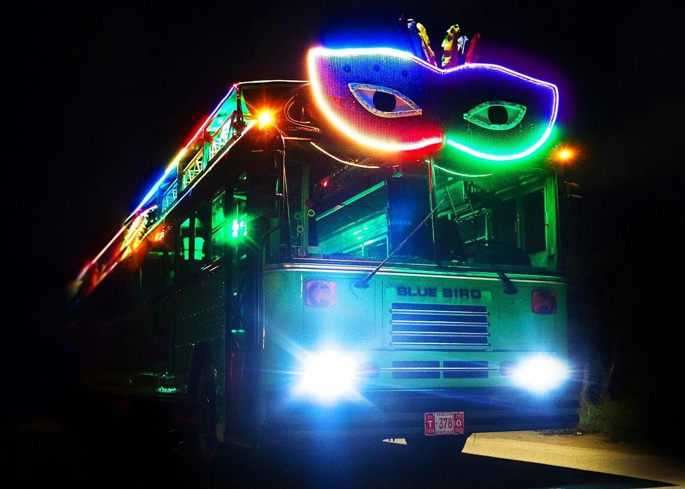 Road Jam party bus at night with a glowing neon masquerade mask on the roof and LED lights.